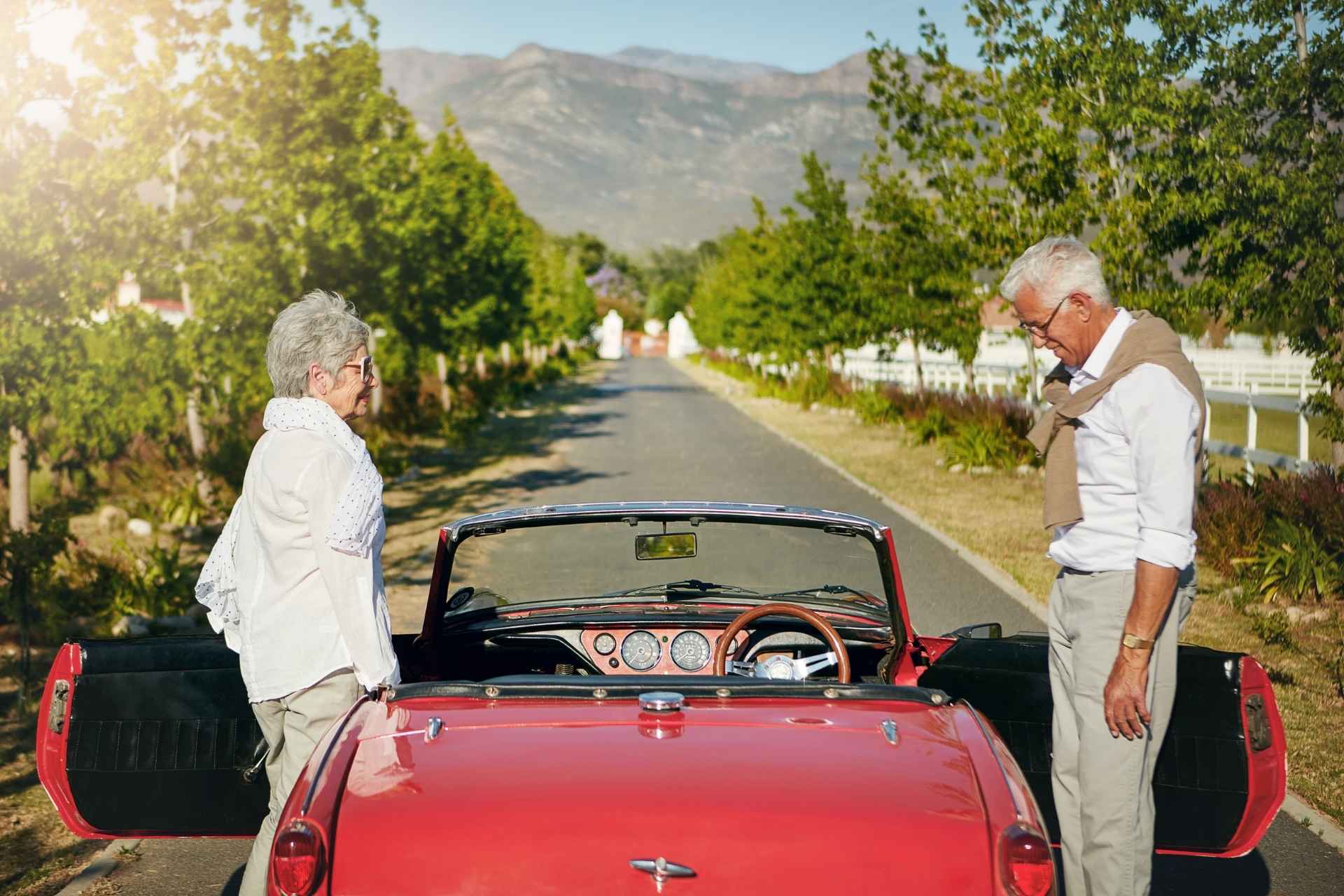 A senior couple getting into a red classic car.